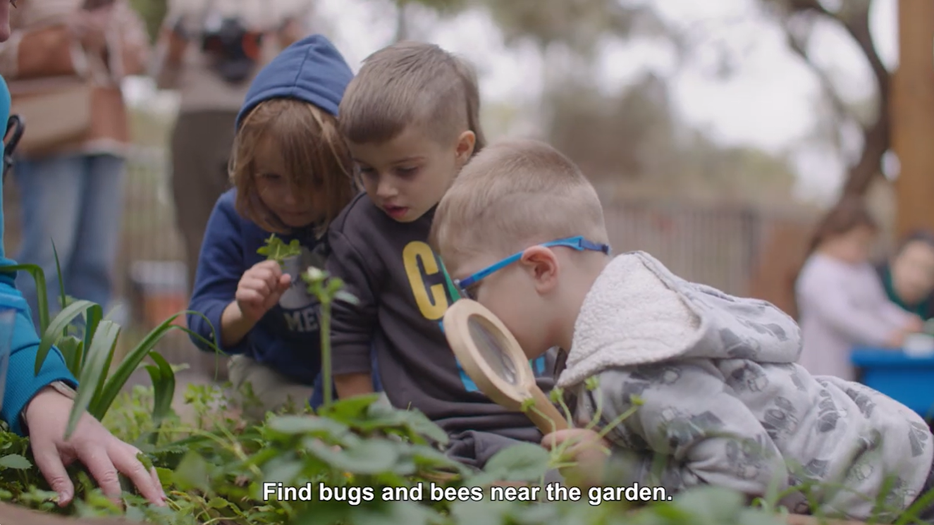 Three children investigating a green garden with magnifying glass