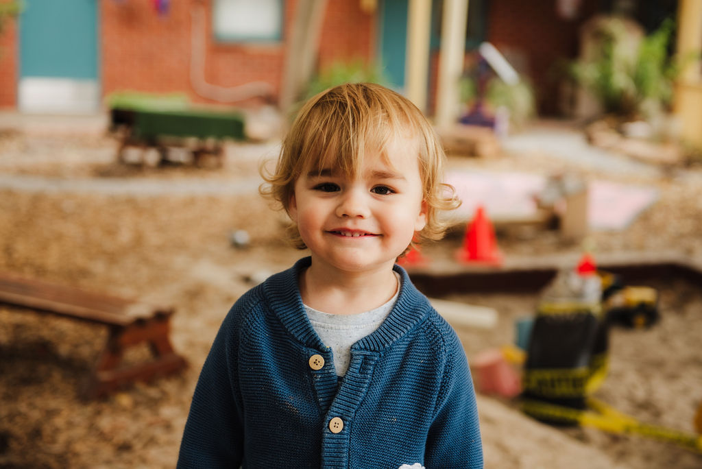 A child in a navy cardigan and blonde curly hair.