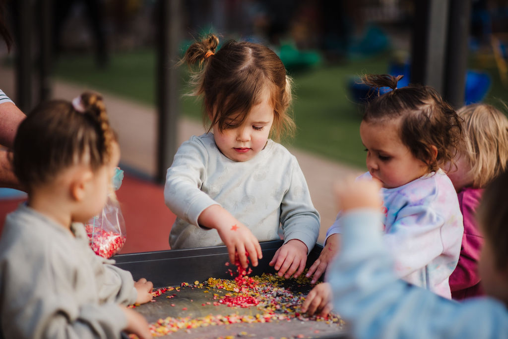 A group of toddlers play with dried lentils and rice in a tough tray